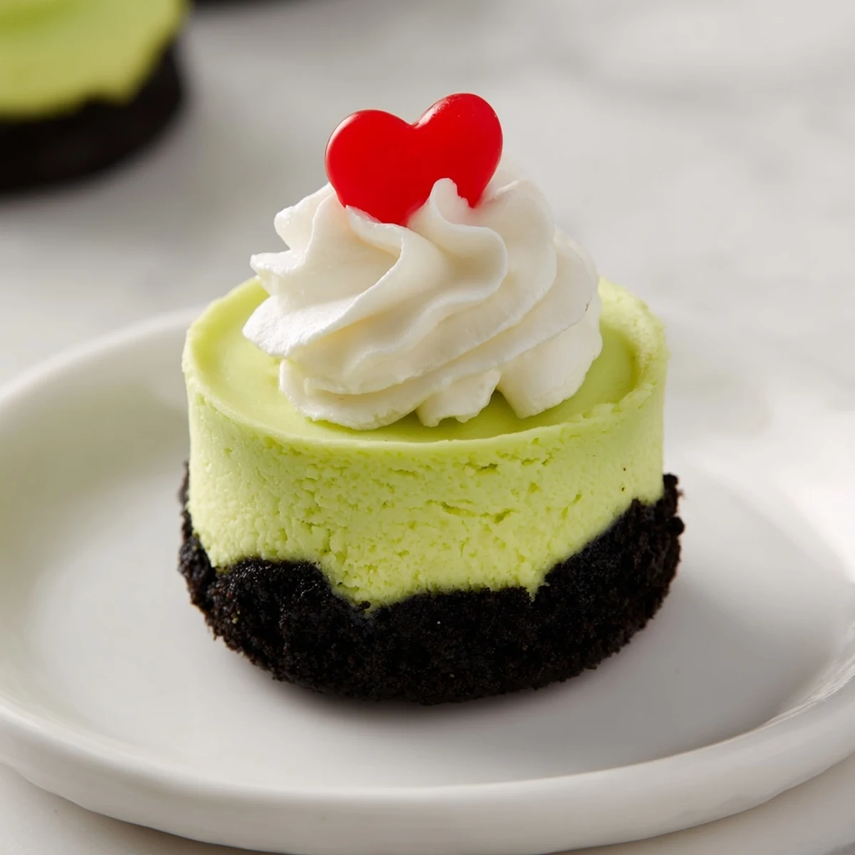 Festive Grinch Mini Cheesecakes, bright green and topped with whipped cream, ready to serve and delight!
