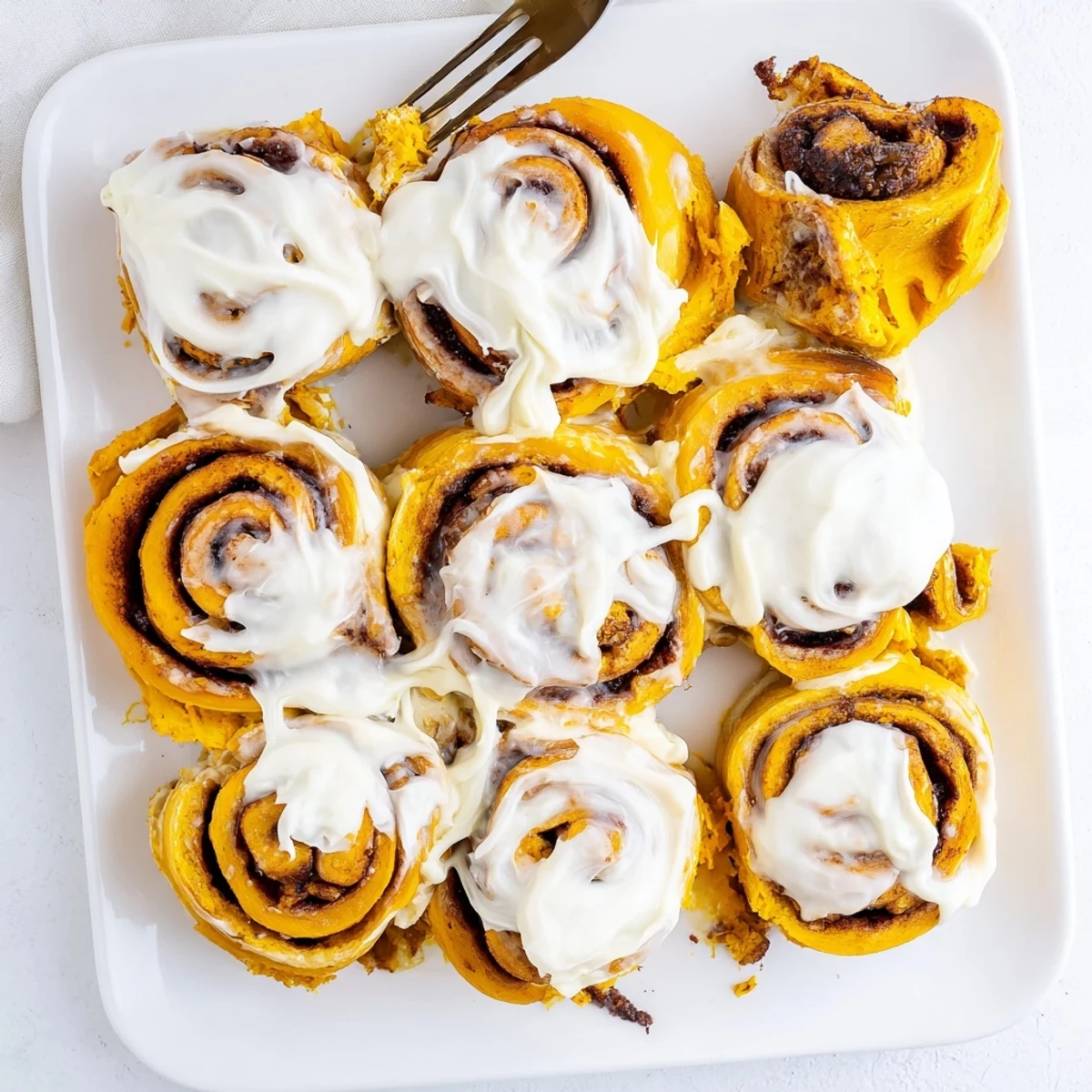 A close-up of soft, pillowy Pumpkin Cinnamon Rolls showcasing the warm pumpkin spice filling and creamy frosting topping.