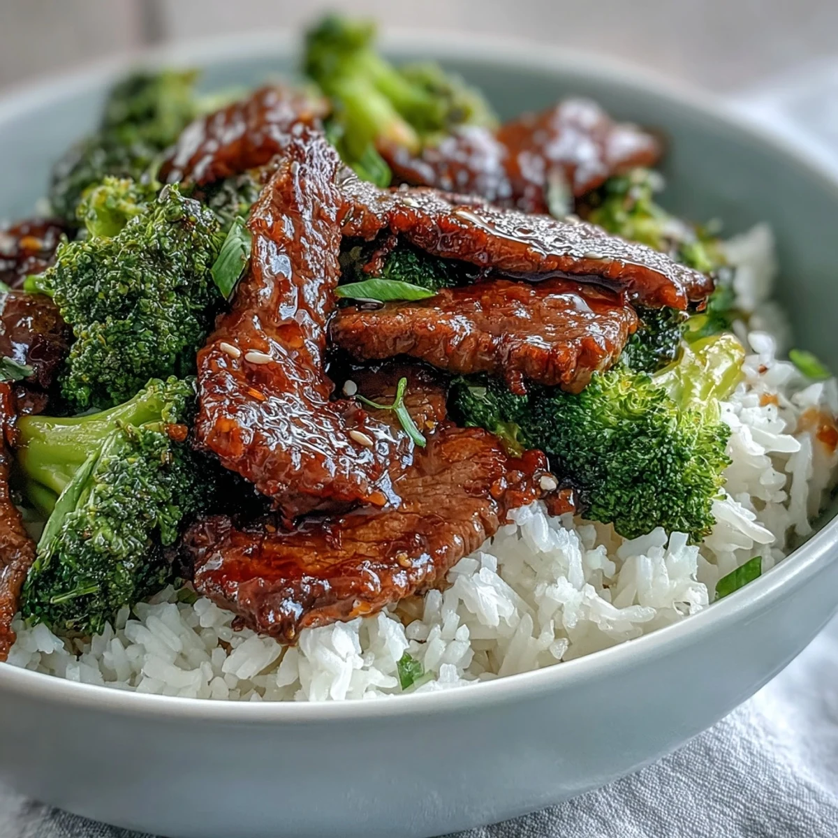Close-up of Beef and Broccoli Bowl showing glossy sauce-coated beef and vibrant broccoli florets next to chopsticks.