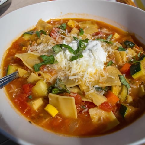 A steaming bowl of veggie-packed one-pot lasagna soup topped with creamy cheese.  