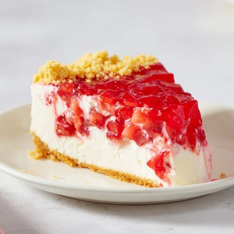 A slice of Strawberry Shortcake Cheesecake with whipped cream and cookie crumble looks delicious.