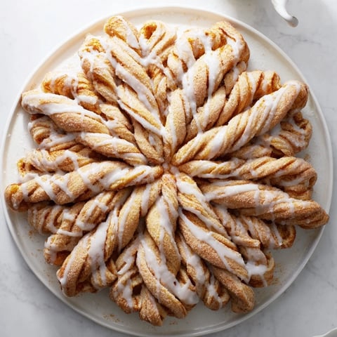 A close-up of a golden Giant Snowflake Sweet Roll, glistening with sweet icing after baking.