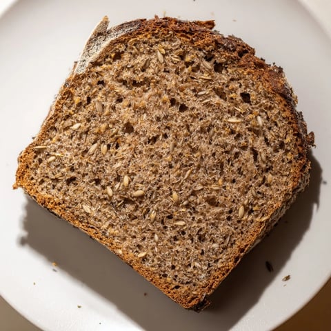 Golden-crusted Latvian Rupjmaize bread awaiting slicing, revealing its soft, dark crumb and toasted caraway seeds.