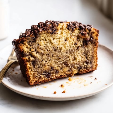 A slice of moist banana bread studded with chocolate chips, served warm on a wooden plate.