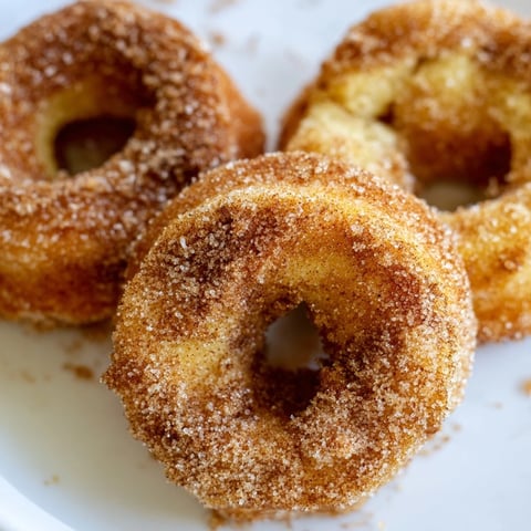 Golden brown Air Fryer Cinnamon Sugar Donuts coated in sparkling cinnamon sugar, served warm on a rustic plate.