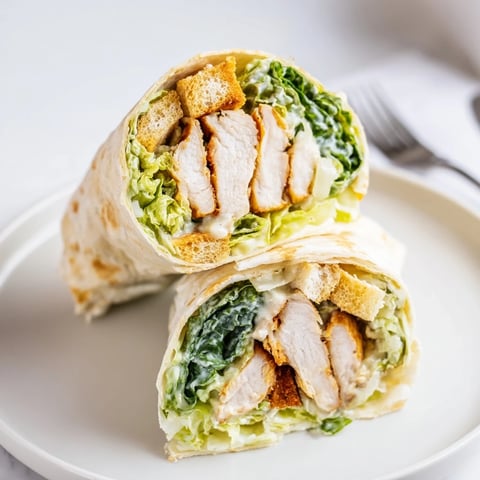 A close-up of a Caesar Chicken Salad Wrap, featuring sliced grilled chicken, crisp romaine, and creamy Caesar dressing nestled in a soft flour tortilla.  