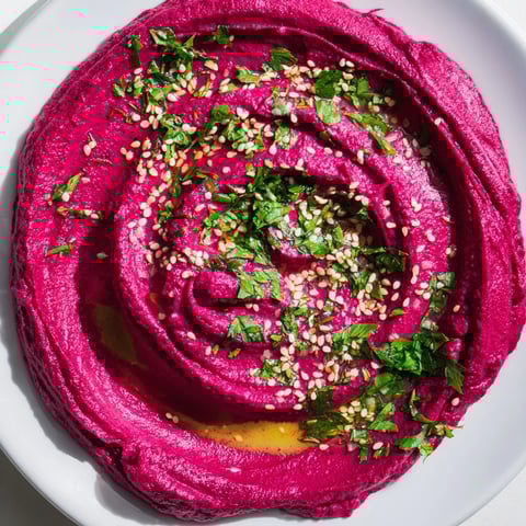 Creamy roasted beet hummus served in a rustic bowl, garnished with parsley and olive oil, alongside pita chips and fresh vegetables for dipping.  