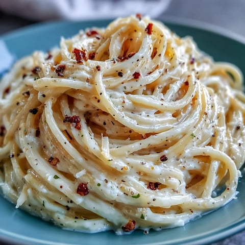 Close-up of Cacio e Pepe showcasing golden strands of spaghetti coated in a creamy Pecorino Romano sauce with freshly cracked black pepper.