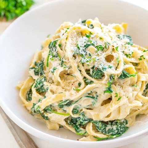 Tender fettuccine coated in creamy Greek Yogurt Spinach Alfredo Pasta, garnished with fresh parsley.