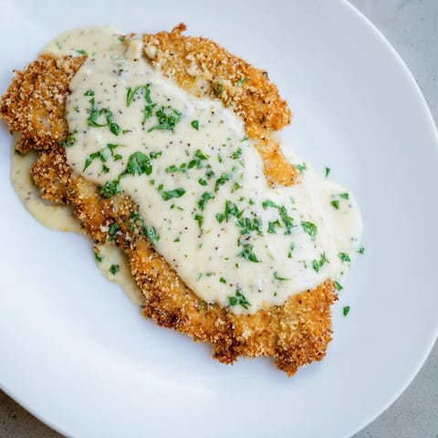 A close-up shot of pan-fried Crispy Chicken with Garlic Cream Sauce, and fresh parsley garnish.