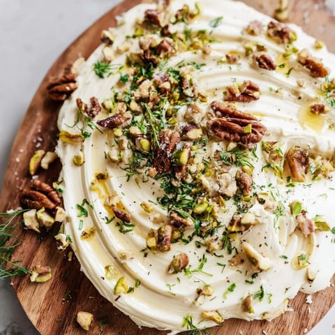 Rustic bread slices beside a Flavored Butter Board topped with fresh herbs, nuts, and sea salt.  