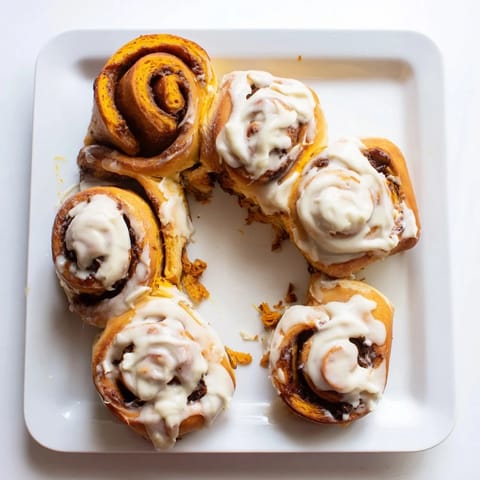 Freshly baked Pumpkin Cinnamon Rolls in a white ceramic dish, with rich cinnamon swirls and a sweet glaze melting down the sides.  