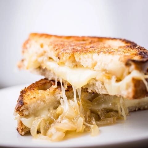 A close-up of a gourmet Caramelized Onion & Gruyère Grilled Cheese beside a fresh green salad.  
