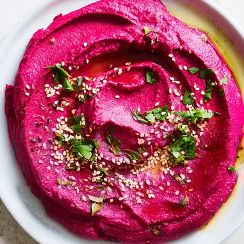 Earthy pink roasted beet hummus spread on toast, topped with sesame seeds and a drizzle of olive oil for a colorful, vegan snack.  