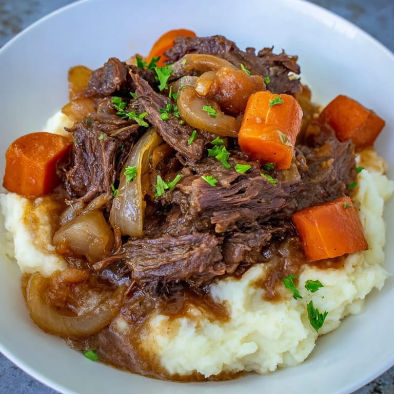 This comforting slow cooker pot roast is served over a bed of creamy, fluffy mashed potatoes.