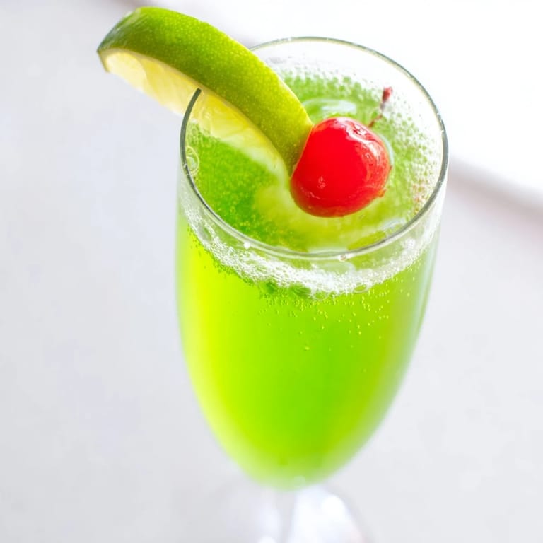 Enjoy the vibrant, non-alcoholic Quick Grinch Mimosa Mocktail, garnished with cherry and lime slices.