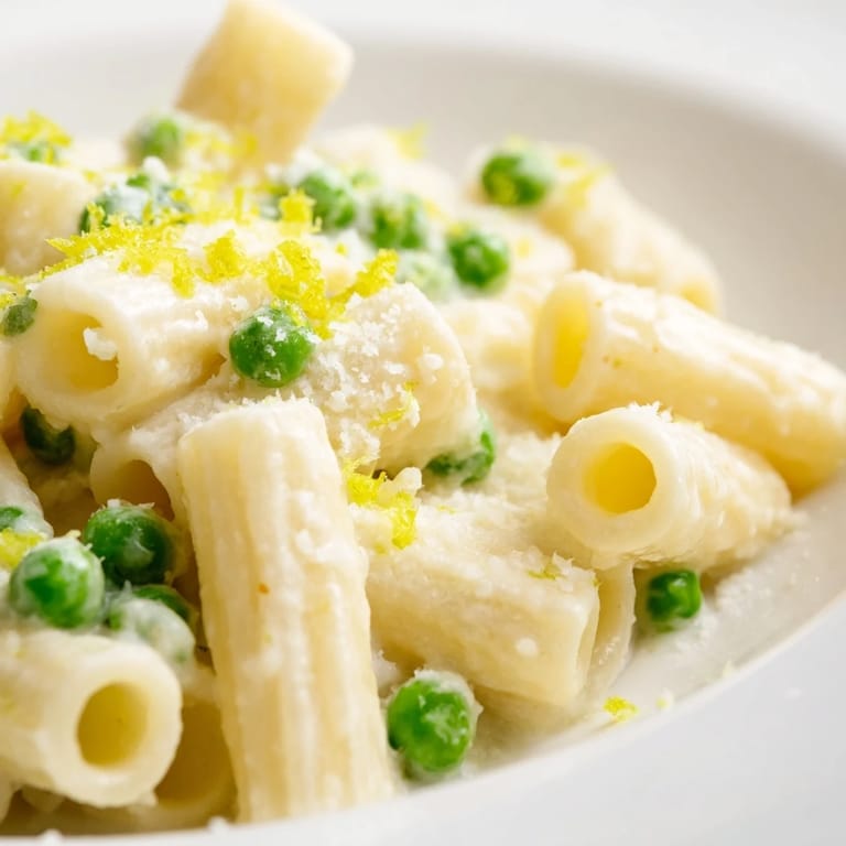 A close-up of vibrant Pea & Lemon Ricotta Pasta, featuring al dente rigatoni, ricotta sauce, and tender green peas.