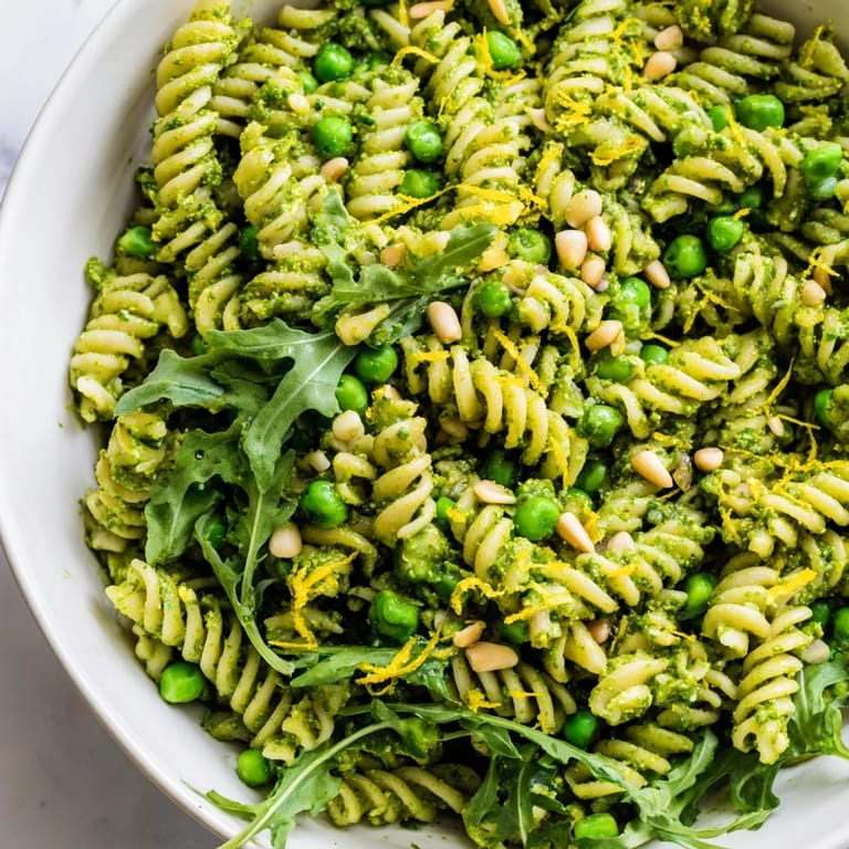 Overhead view of Spring Green Pesto Pasta Salad with colorful ingredients like peas, lemon zest, and peppery baby arugula.
