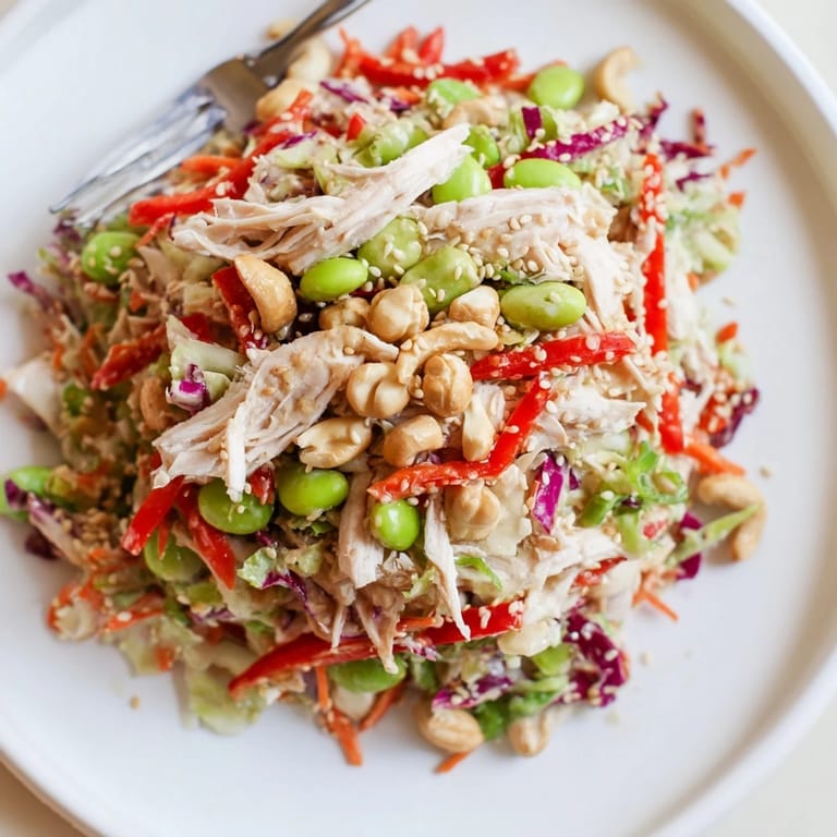 Freshly prepared Edamame Crunch Chicken Salad served in a white bowl, featuring edamame, red bell pepper, and toasted sesame seeds.