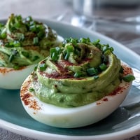 Green deviled eggs with avocado filling, garnished with smoked paprika and fresh chives for a colorful appetizer.  